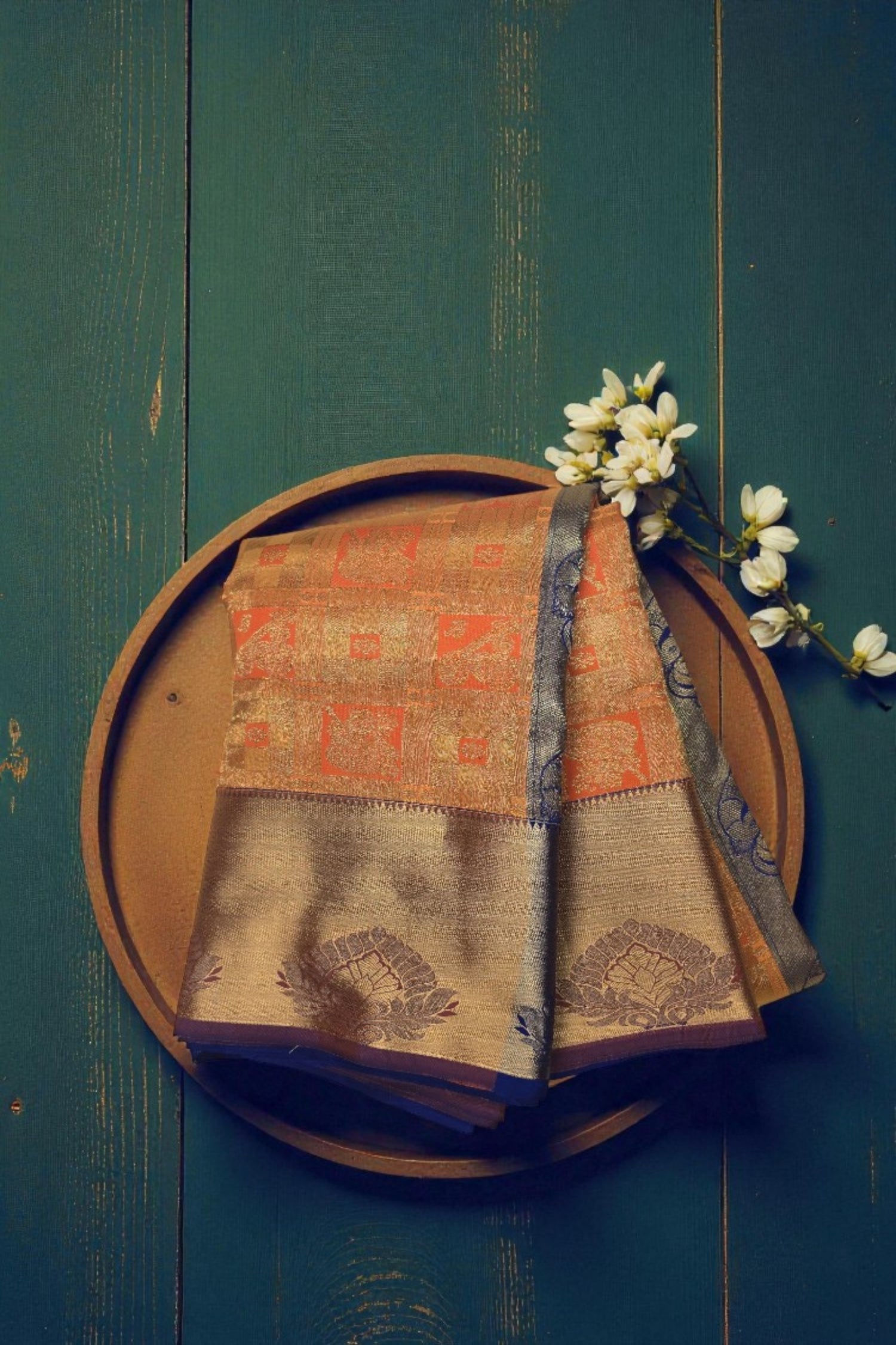 Traditional saree with a wooden plate and white flowers on a dark green background