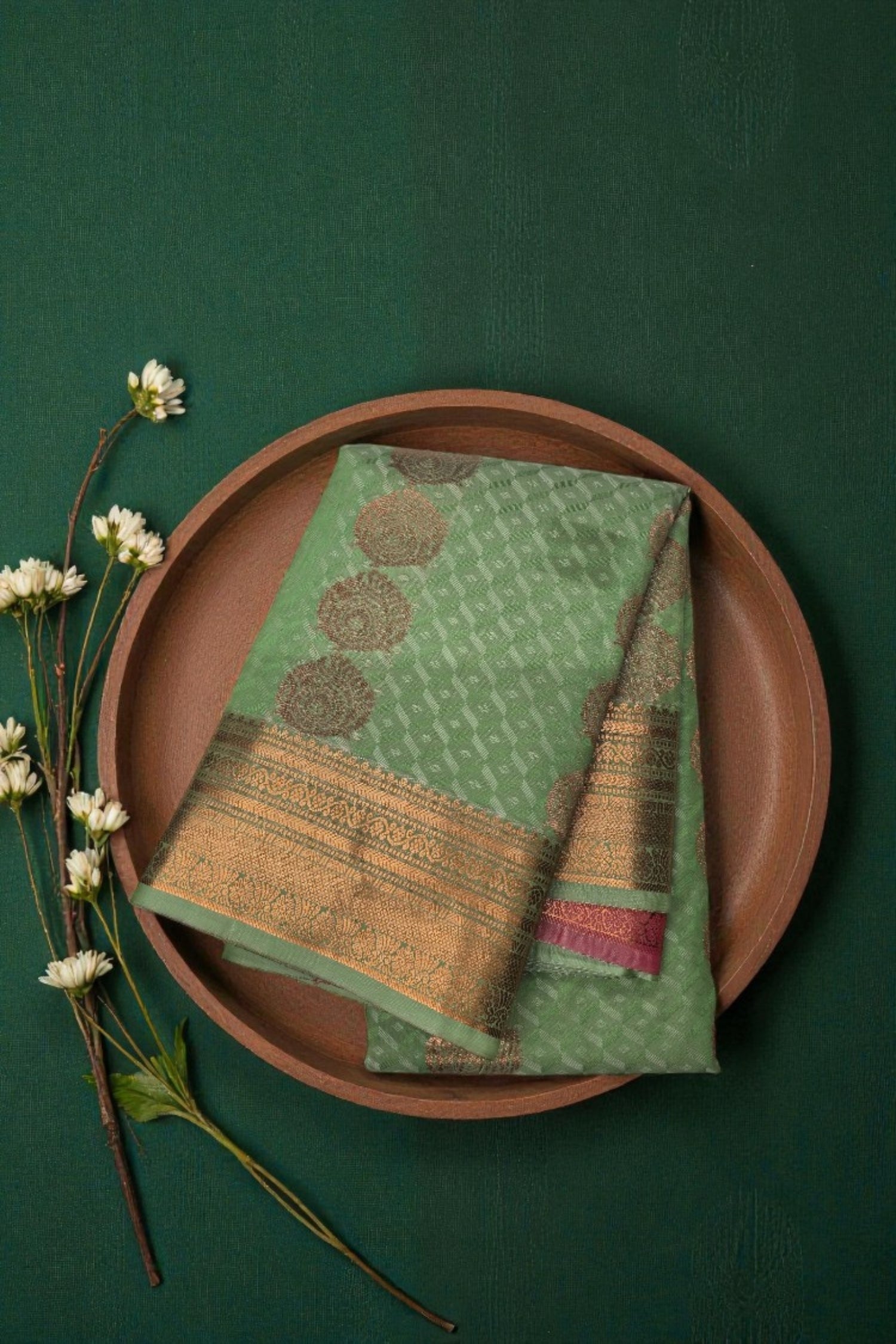 Green and gold patterned fabric on a brown plate with white flowers on a green background