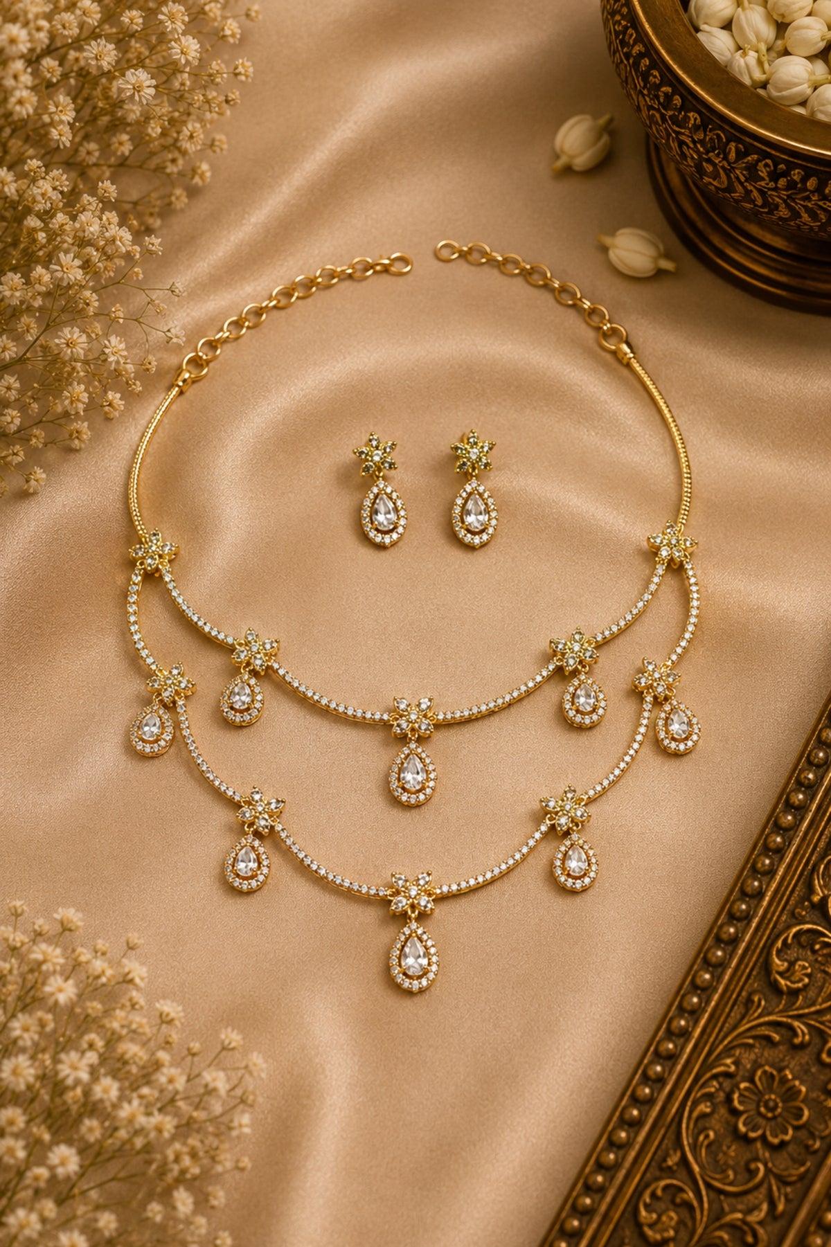 Gold necklace and earrings on a beige fabric background with dried flowers.