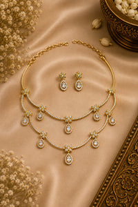 Gold necklace and earrings on a beige fabric background with dried flowers.