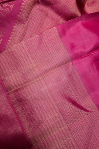 A close-up of a pink silk saree or fabric, showing the woven body with fine gold zari detailing and a solid pink border.