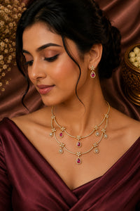 Woman wearing a gold necklace with red gemstones against a brown fabric background