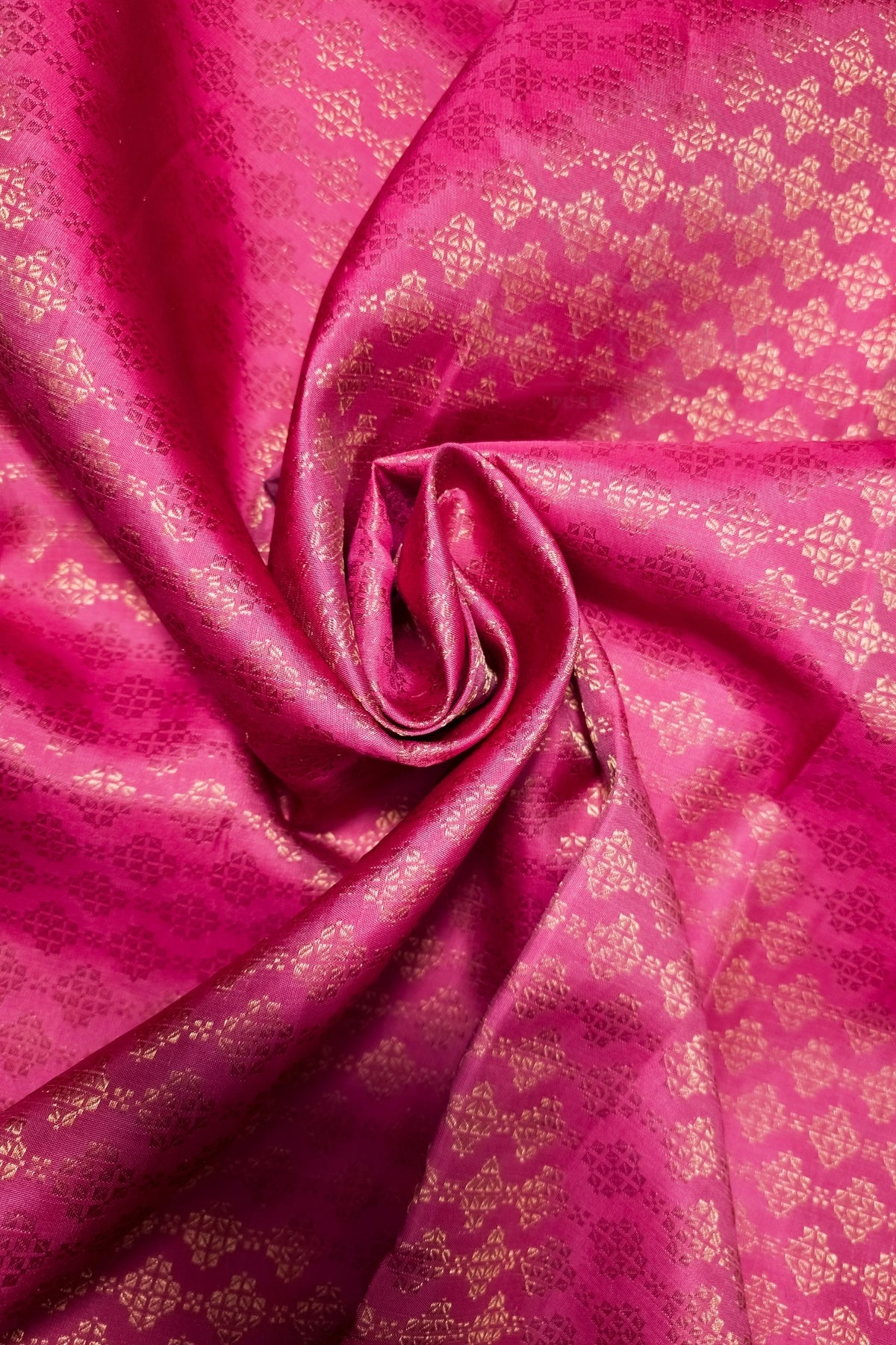 A close-up of bright pink fabric with a metallic gold woven floral pattern, arranged in a spiral drape.