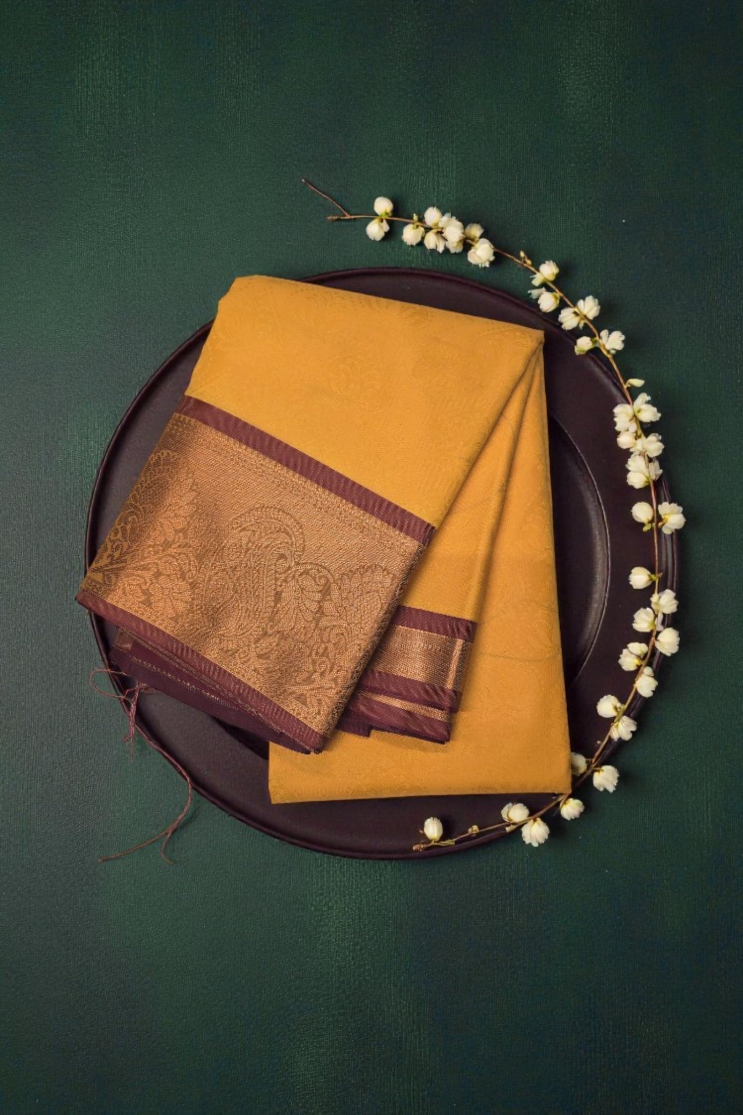 Mustard yellow saree with brown border on a dark green background