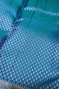 A close-up of a blue and teal patterned fabric with metallic silver woven motifs and a decorative border.