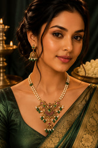 A woman wearing an ornate gold and green traditional necklace with matching earrings, styled with a dark green saree in a warm, elegant setting.