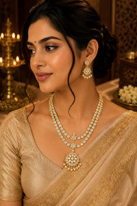 A woman wearing a traditional Indian outfit in beige and gold, showcasing a double-strand gold and white stone necklace with a large matching pendant, along with matching earrings.