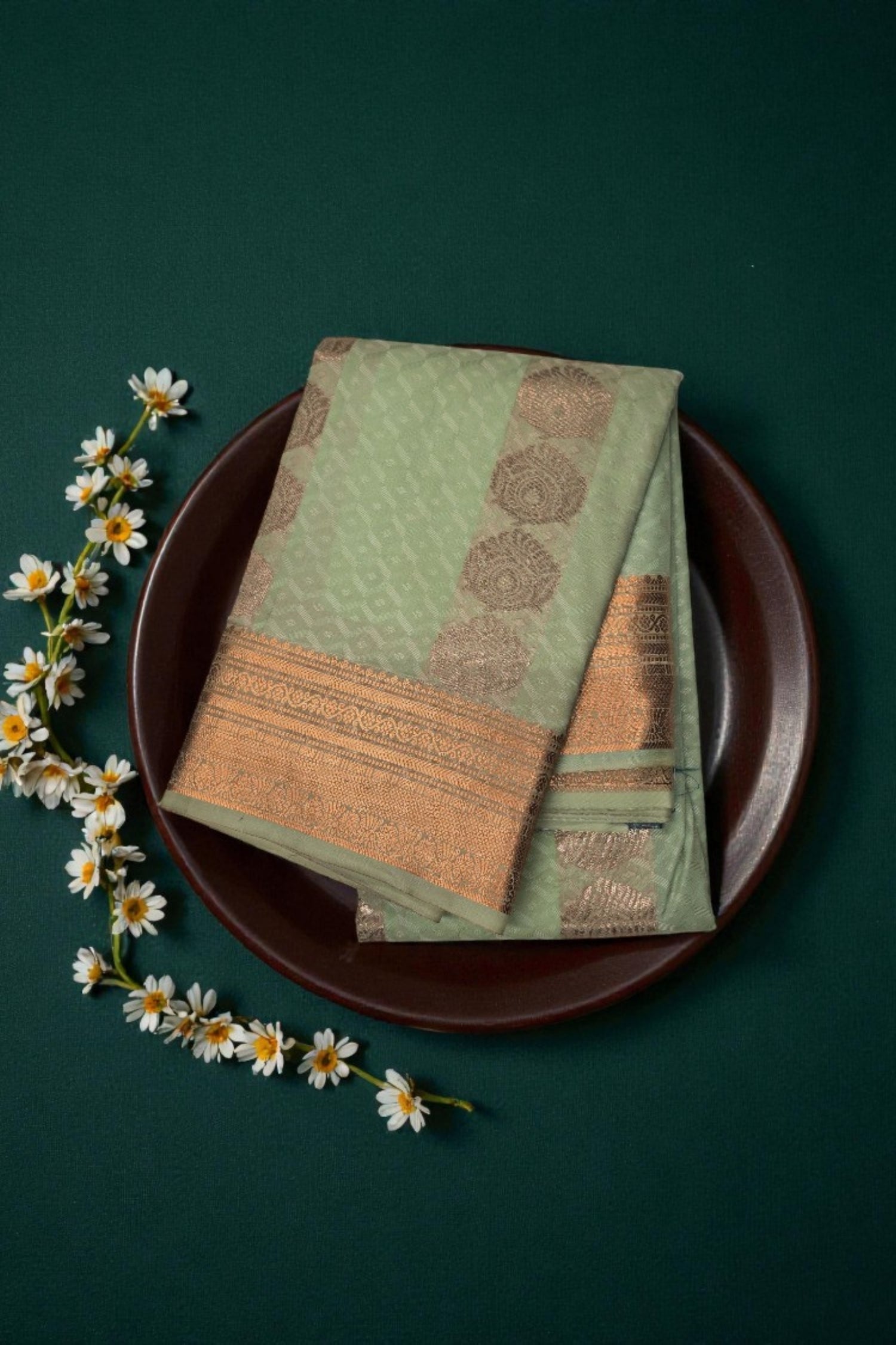 Green and brown patterned fabric on a dark green background with white flowers.