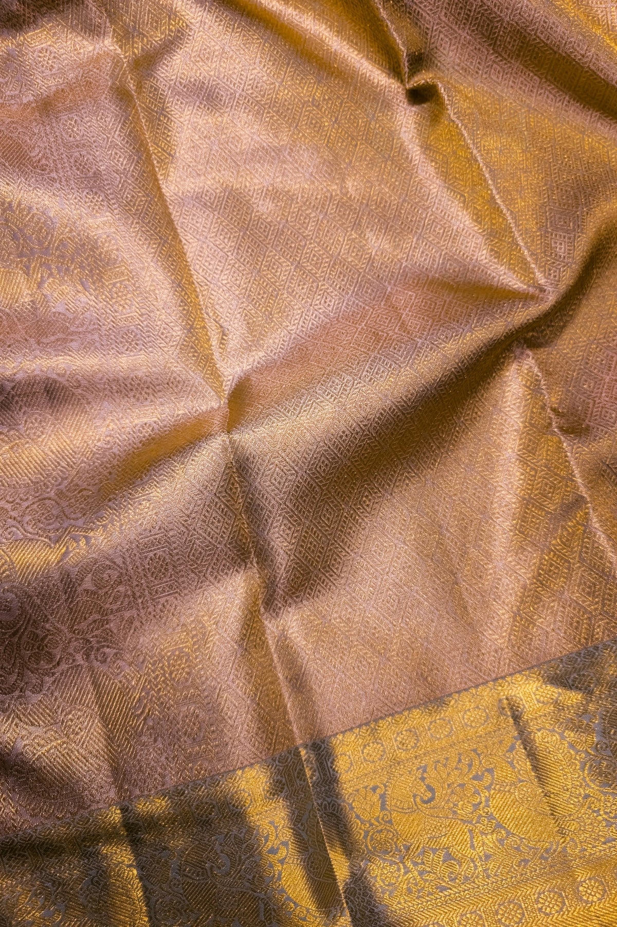 A close-up of a draped metallic gold fabric with a subtle woven pattern and a decorative border at the bottom.