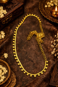 A Waist chain with small beaded drops along the front, arranged in an oval shape on a dark brown textured surface with decorative floral and brass props.
