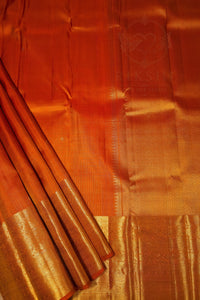 A close-up of an orange silk saree with a wide gold zari border and pallu, showing its texture and sheen.
