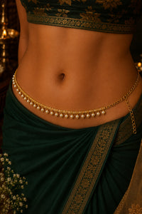 A close-up of a model's waist wearing a gold chain belly chain decorated with small white pearls, styled with a dark green sari.