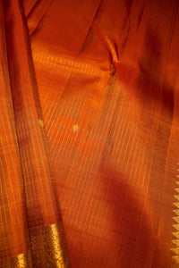 Close-up of an orange silk saree fabric with fine gold zari stripes, a gold border, and small gold motifs.