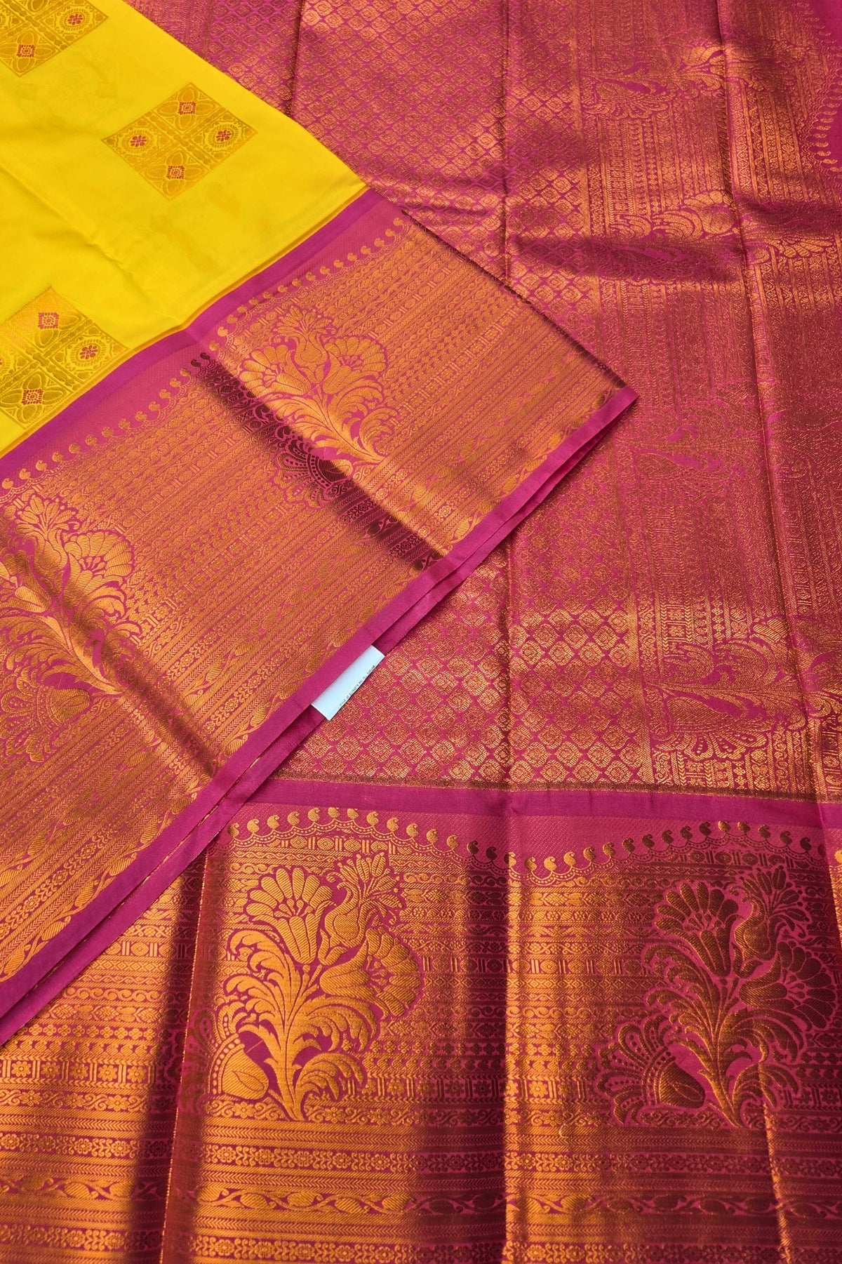 Traditional saree with intricate patterns in yellow, pink, and gold on a plain background