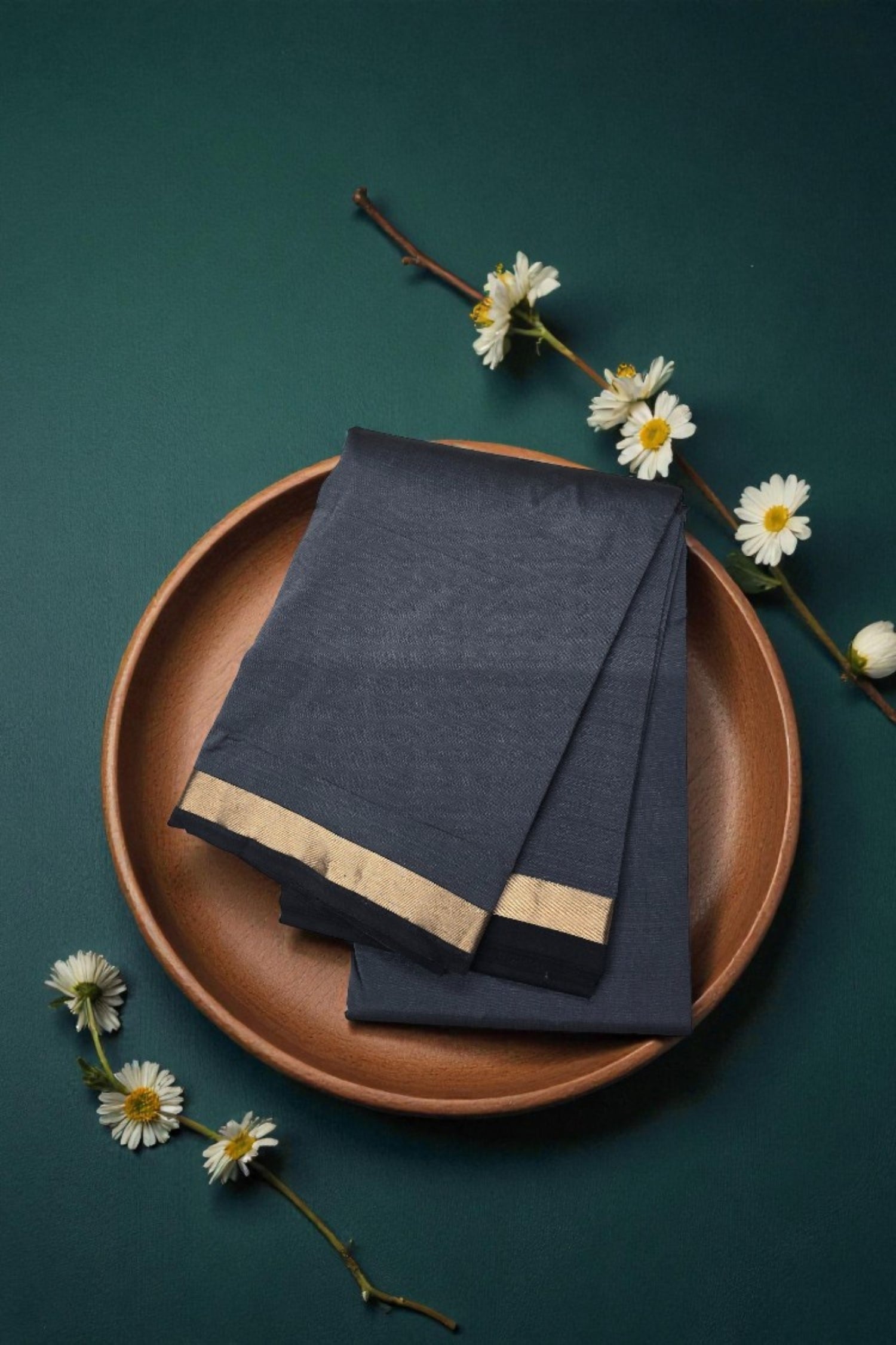 Dark blue napkin with gold trim on a brown plate against a green background
