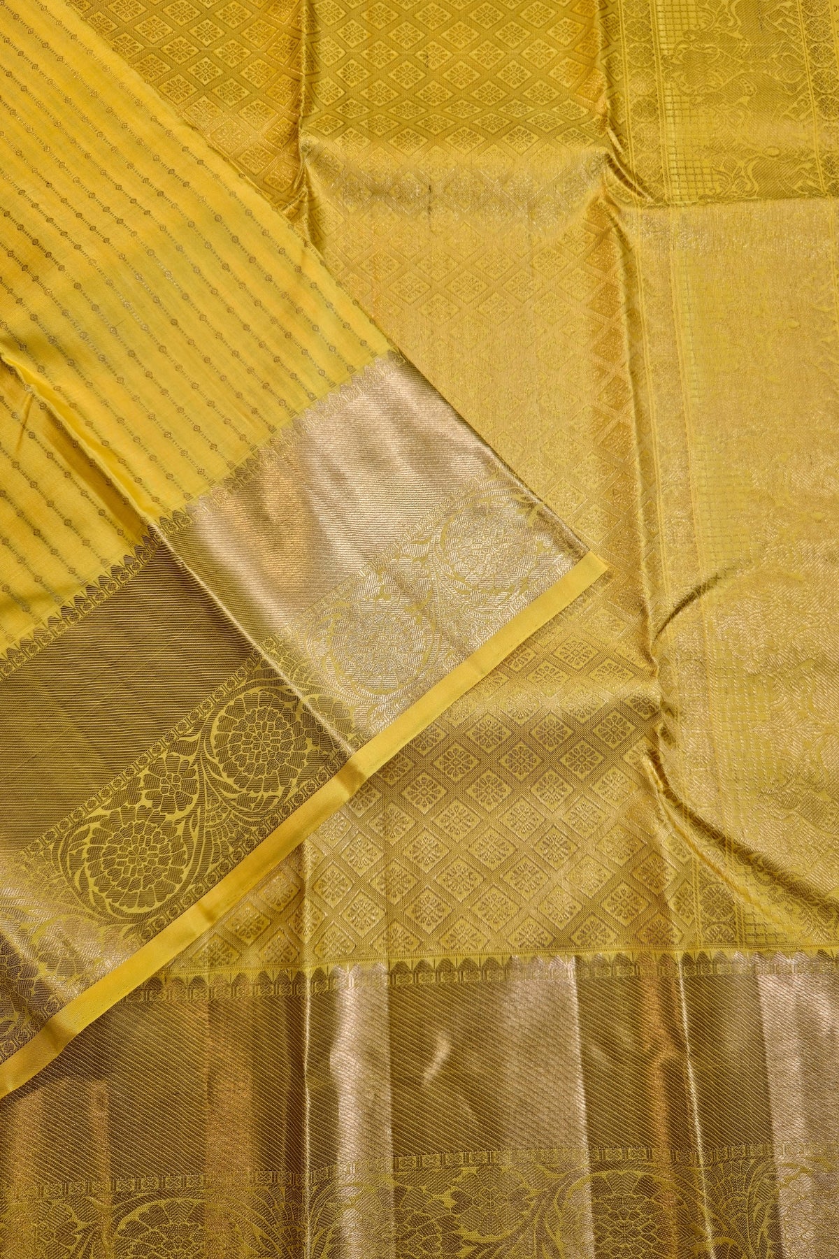 A close-up of a yellow and gold zari woven fabric, likely a saree or textile, showing the detailed patterned body and a wide metallic gold border.