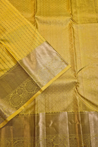 A close-up of a yellow and gold zari woven fabric, likely a saree or textile, showing the detailed patterned body and a wide metallic gold border.