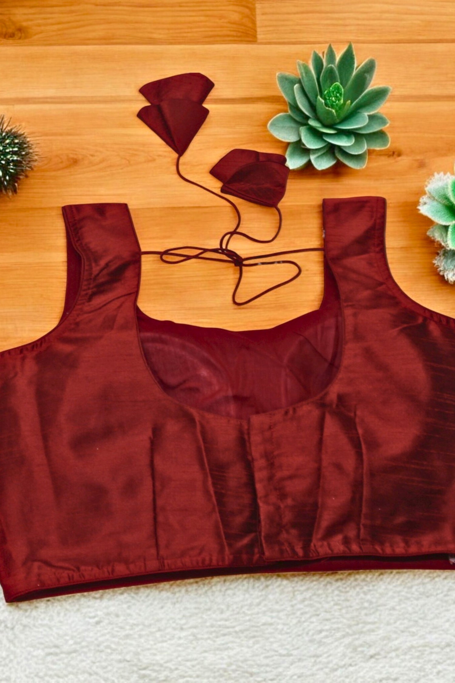Red satin top on a wooden surface with small plants.