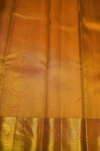 A close-up of a golden-yellow silk fabric, likely a saree, featuring a wide decorative border with woven floral motifs and a smooth central body.