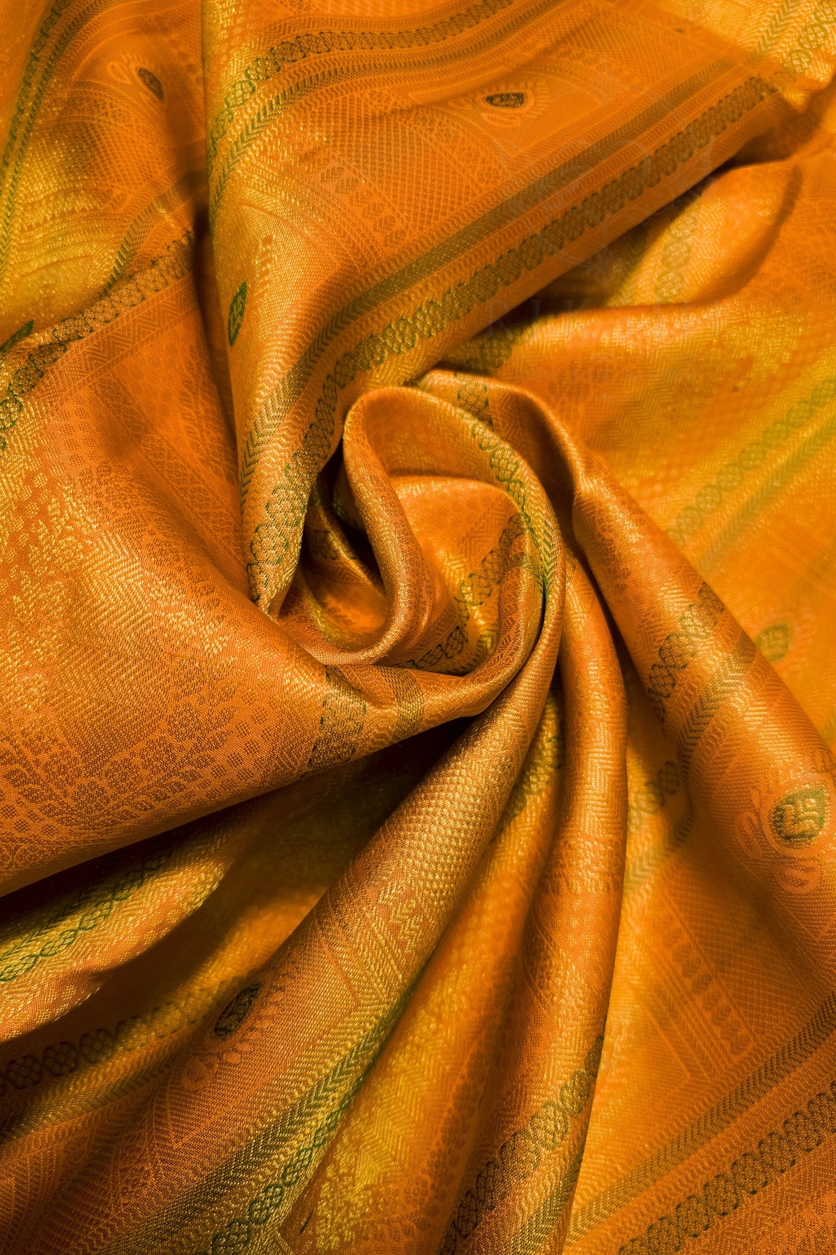 A close-up of draped golden-yellow fabric with woven geometric patterns and subtle green accents, arranged in soft folds.