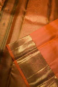 Close-up of an orange and gold zari woven fabric, likely a silk saree, showing the rich metallic sheen and detailed brocade patterns.