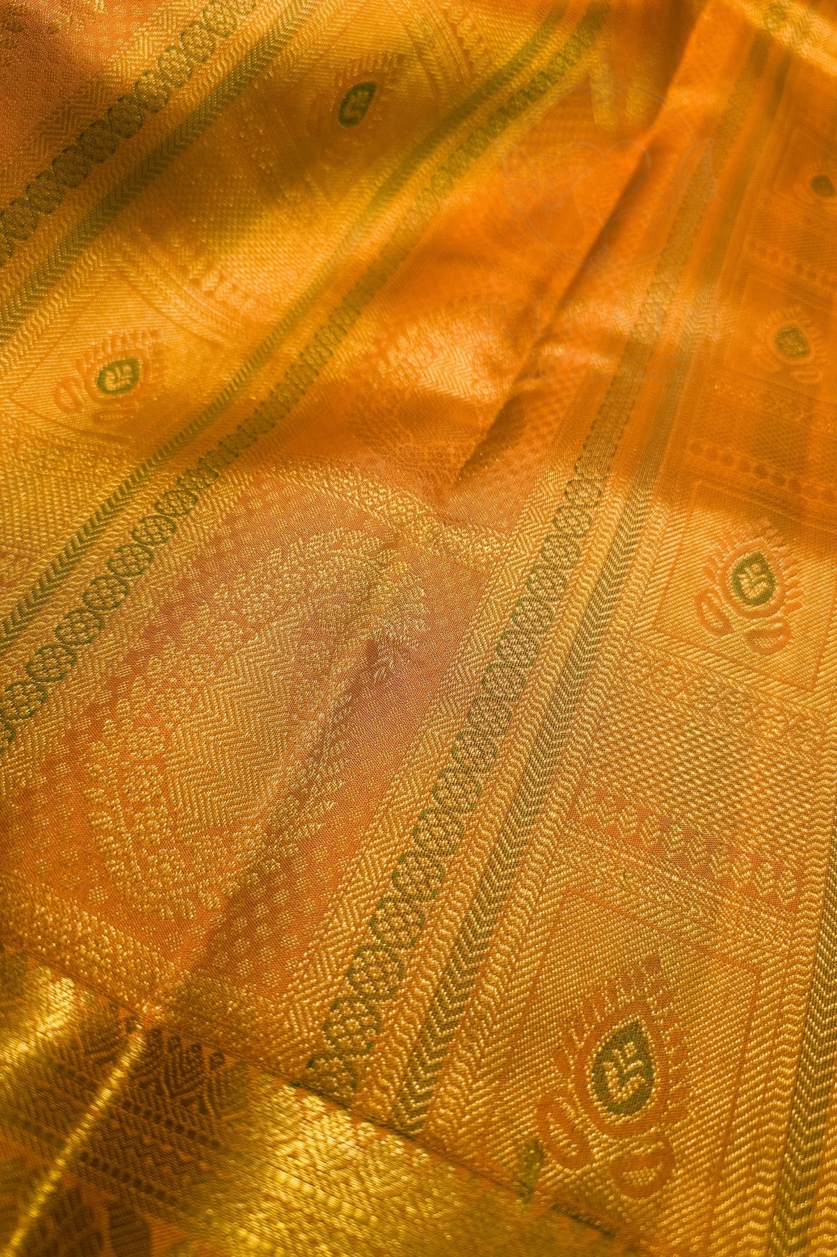 A close-up of a golden-yellow silk fabric with intricate metallic zari woven patterns and borders.