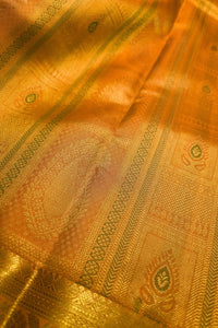A close-up of a golden-yellow silk fabric with intricate metallic zari woven patterns and borders.