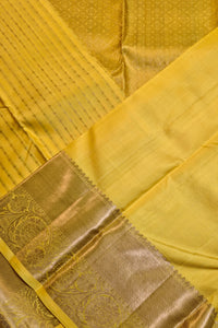 A close-up of a yellow silk saree with a wide metallic gold border featuring intricate woven floral patterns.