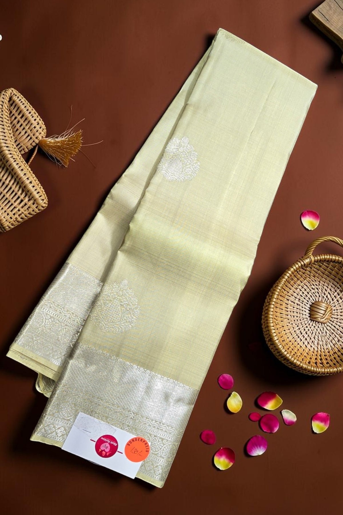 Light green fabric with white floral patterns on a brown surface with wicker baskets and rose petals.