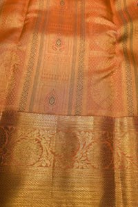 Close-up of a woven textile with a warm orange-pink base and extensive metallic gold zari patterns, including a wide decorative border.