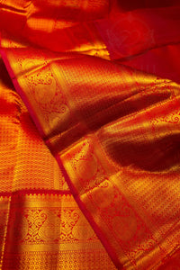 A close-up of a rich red and gold silk saree with intricate zari woven patterns and a border design.