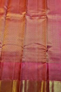 A close-up of a pink and gold zari woven fabric, likely a silk saree or textile, showing the texture, sheen, and metallic border details.