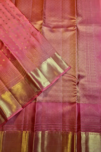 A close-up of a pink and gold zari silk saree, showing the woven fabric texture, metallic gold borders, and delicate gold dot patterns on the pallu.