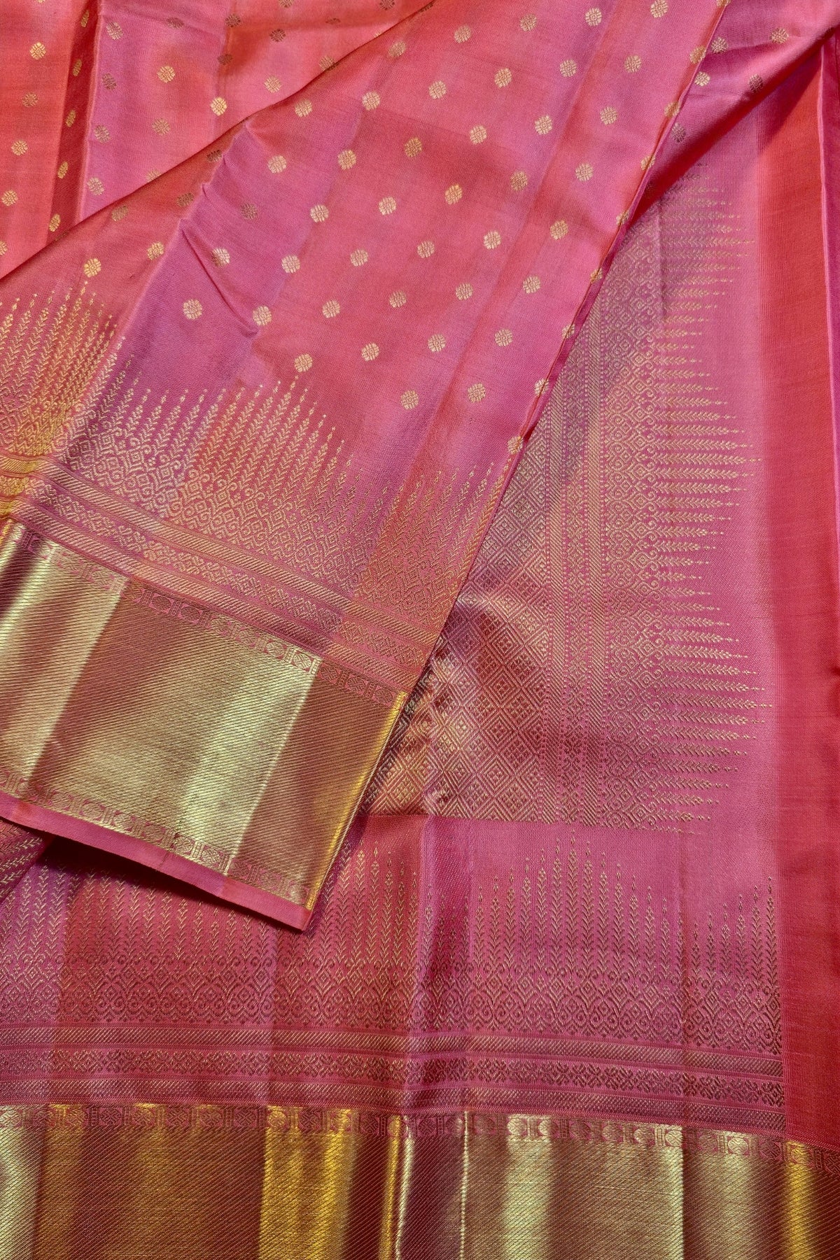 A close-up of a pink silk saree with gold zari woven patterns, featuring a dotted body, a wide gold border, and a detailed gold pallu.
