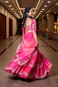 Woman in a pink traditional outfit with floral patterns in an indoor setting.