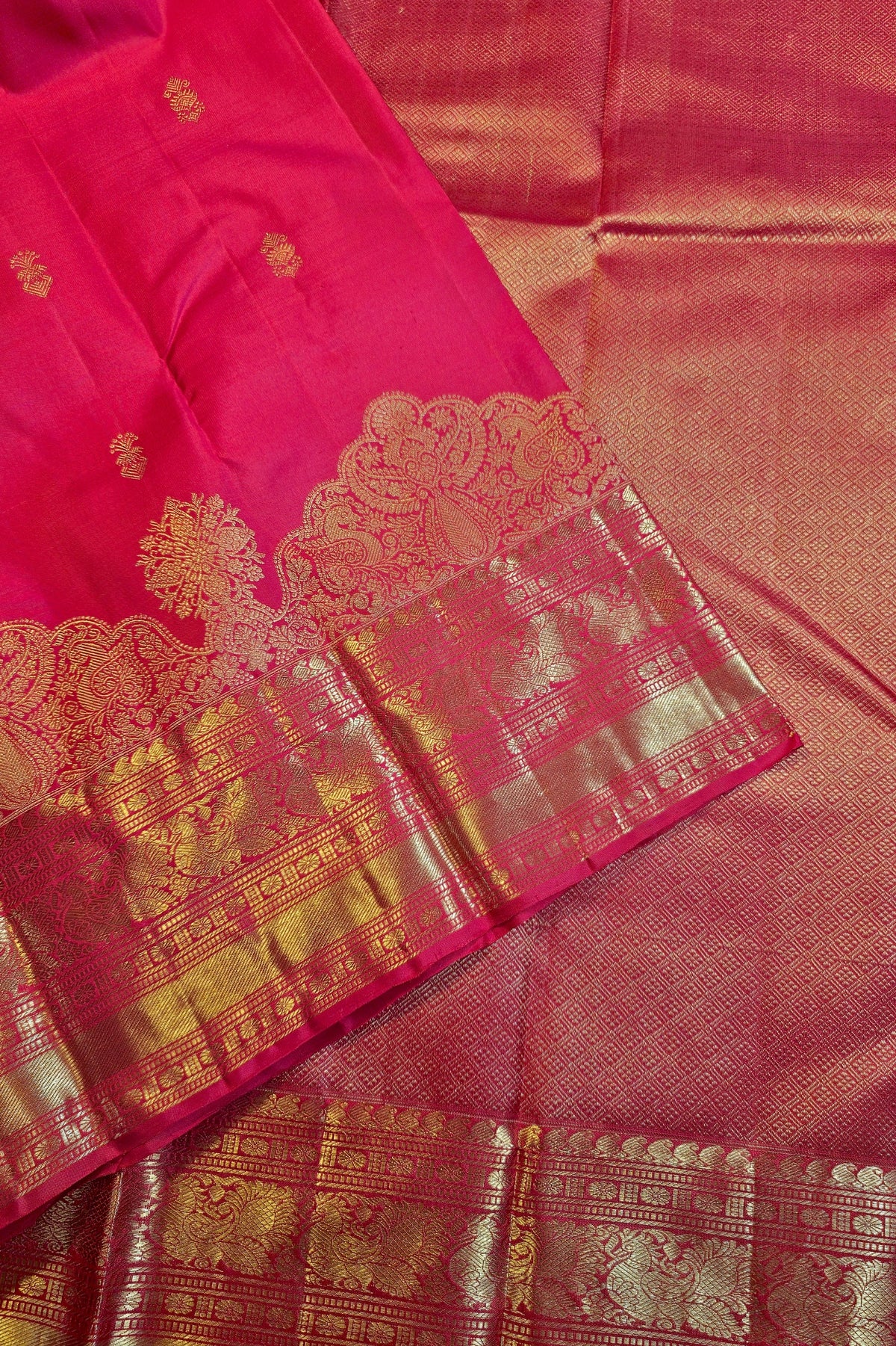 A close-up of a pink silk saree with a wide gold zari border and intricate metallic gold motifs.