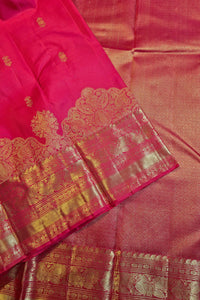 A close-up of a pink silk saree with a wide gold zari border and intricate metallic gold motifs.