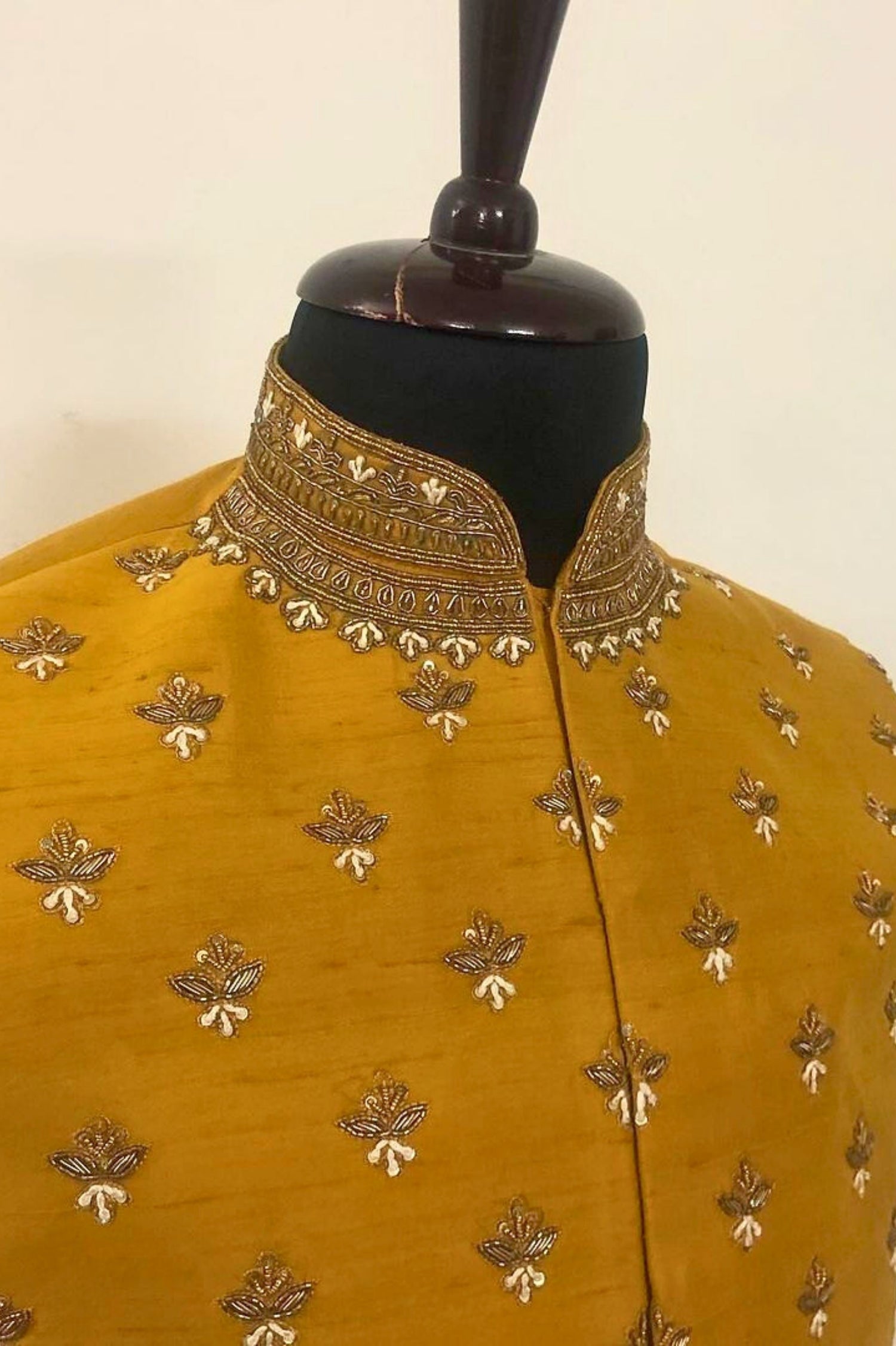 Mustard yellow garment with gold embroidery on a mannequin against a beige background