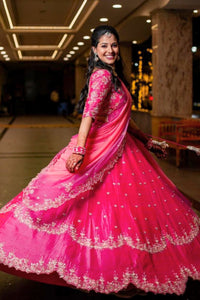 Woman in a pink traditional outfit with intricate designs in an indoor setting.
