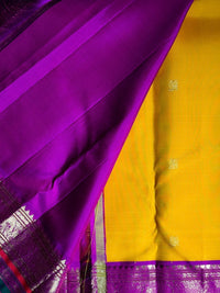 A close-up of a traditional sari with a bright yellow body and a rich purple border, featuring small gold floral motifs on the yellow fabric.
