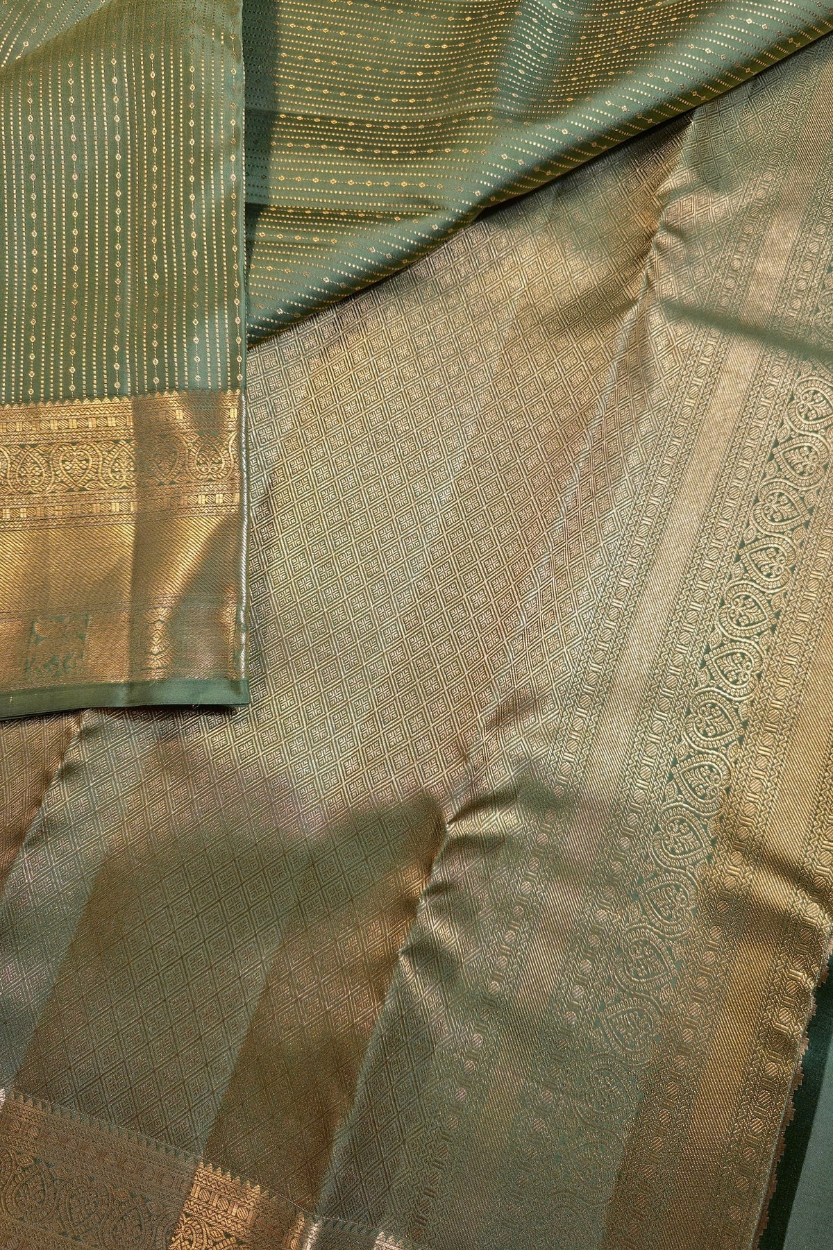 Close-up of a woven fabric textile with a sage green body, gold zari metallic patterns, and a matching green border with gold detailing.