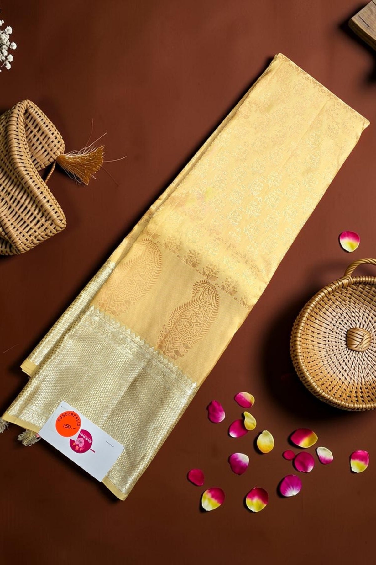 Beige fabric with embroidery on a brown surface with wicker baskets and flower petals.