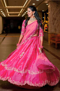 Woman in a pink traditional outfit with intricate designs in an indoor setting.