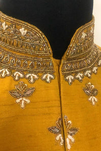 Mustard yellow fabric with intricate gold embroidery on a black background