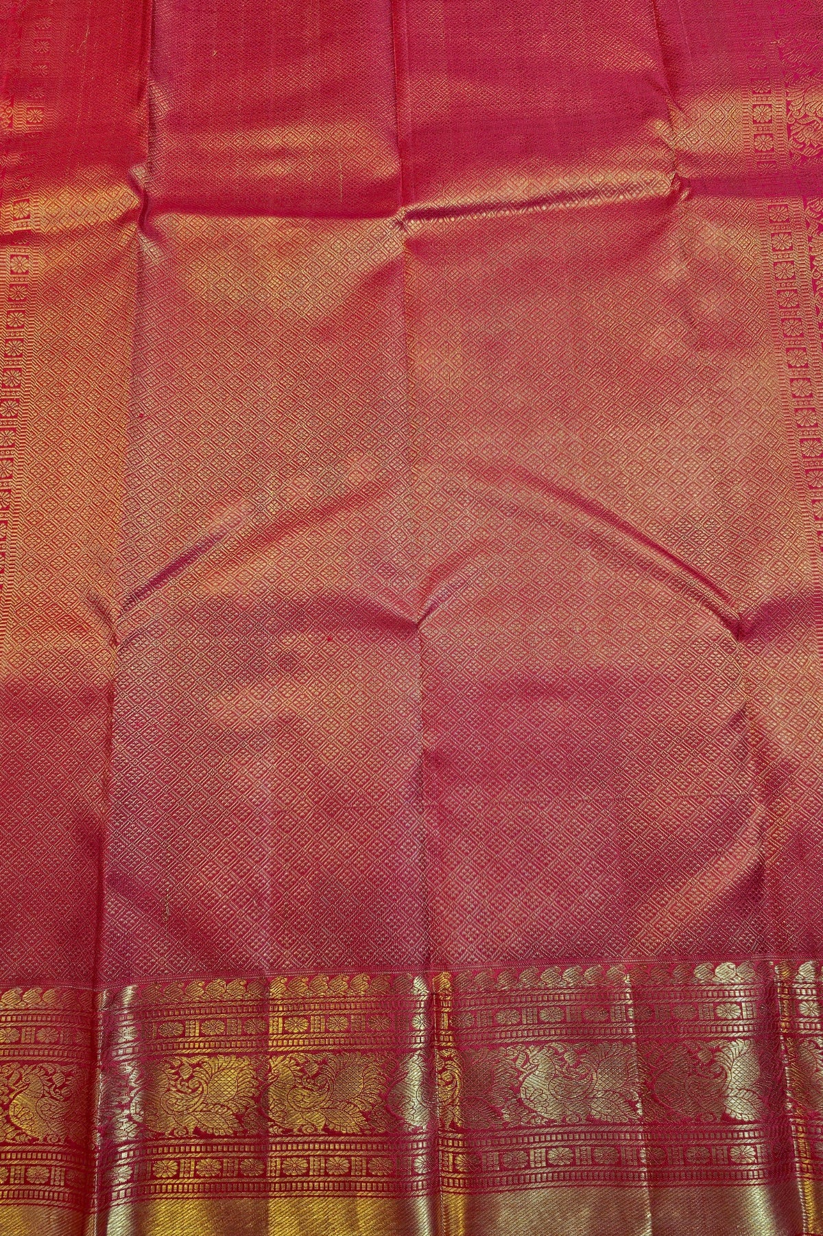 A close-up of a pink silk saree fabric with a wide gold zari border and intricate woven patterns.
