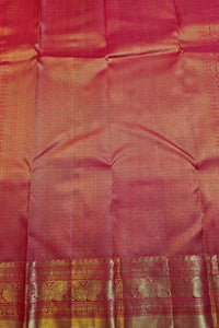 A close-up of a pink silk saree fabric with a wide gold zari border and intricate woven patterns.