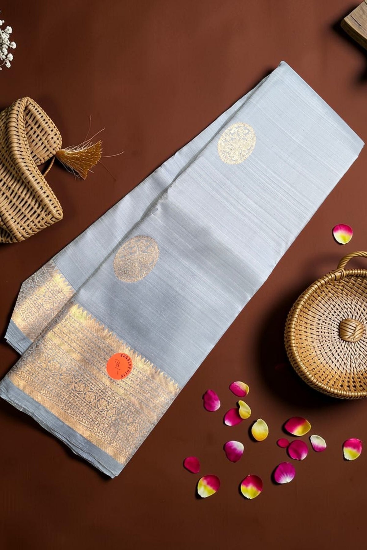 Light blue saree with gold patterns on a brown surface with wicker basket and rose petals.