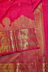 A close-up of a rich magenta pink silk saree with intricate gold zari woven borders and traditional motifs.