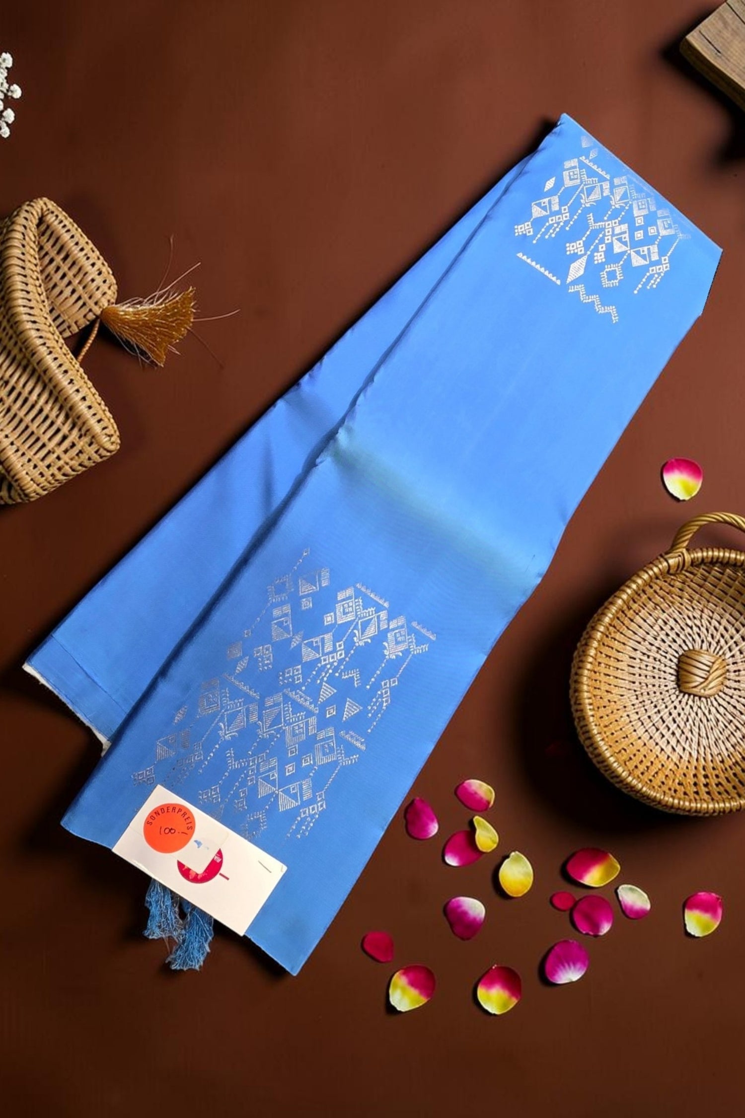 Blue fabric with white floral patterns on a brown surface with wicker baskets and flowers.