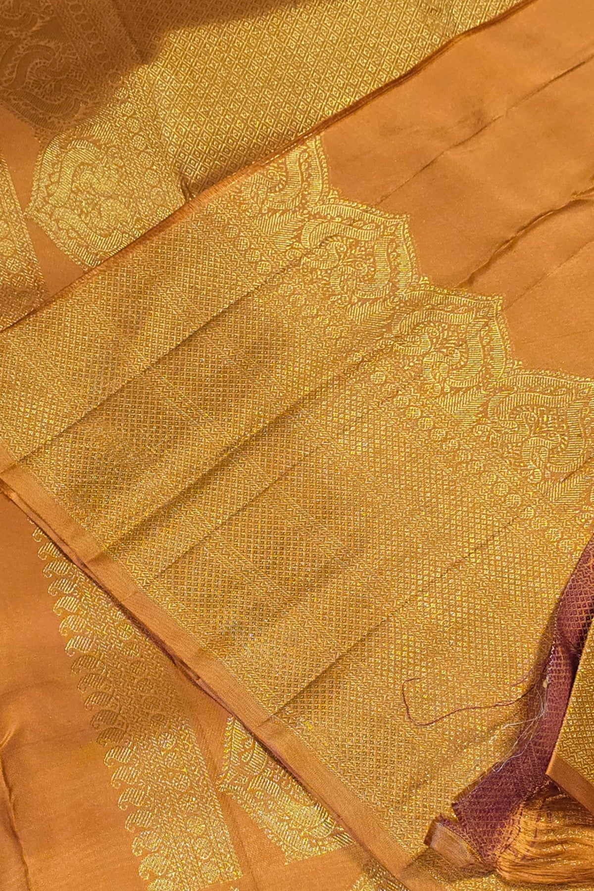 Close-up of a gold saree with intricate patterns on a brown background